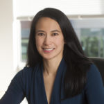 A woman with long black hair sitting in front of a window.
