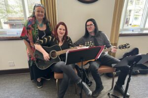 Three people sitting on a bench with guitars
